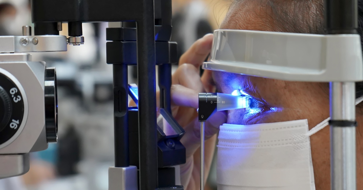 An ophthalmic professional examines a man's eyes with a tonometer. It shines a blue light into his eyes.