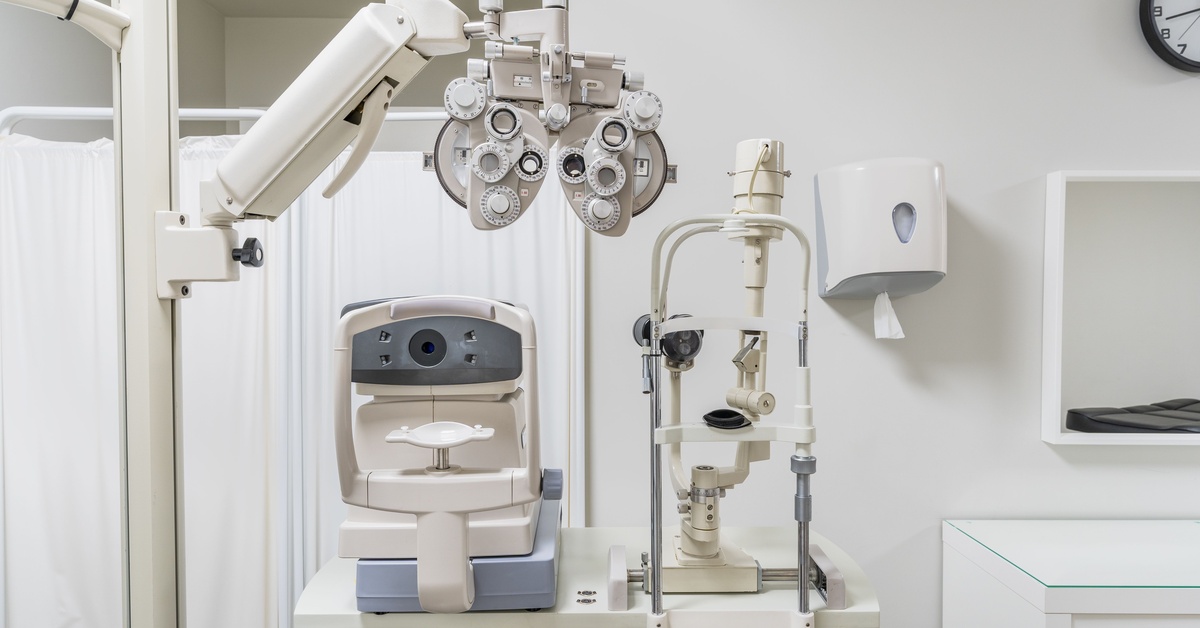 A medical office has eye exam equipment and a face rest of a mobile desk. There is a medical curtain in the background.