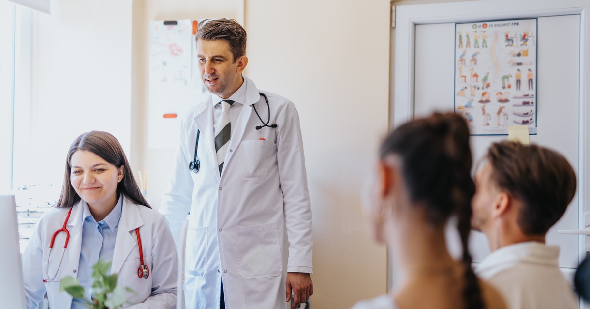 Two medical professionals interact warmly with two patients seated across from them inside a bright clinic.