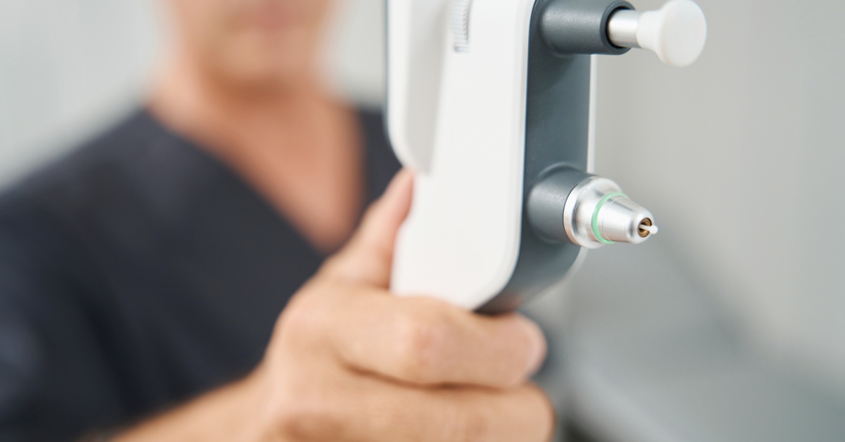 A close-up of a person holding a tonometer in a well-lit environment, showing the device off in detail.