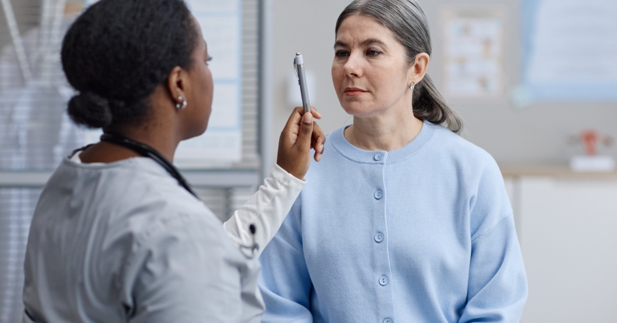 A medical professional holding a pen while performing an eye movement examination on a seated patient in an office.