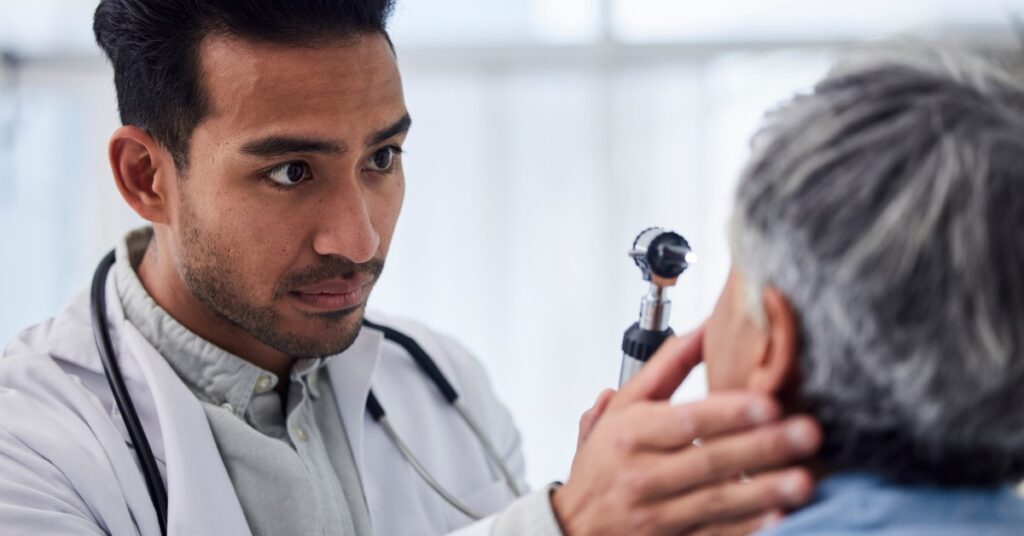 A medical professional performs an eye assessment on an older gentleman in a clinic using an instrument with a light.