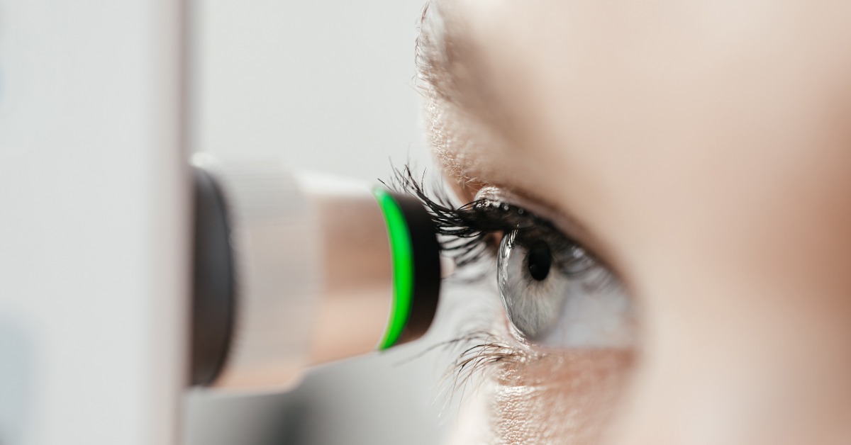 An extreme close-up of a tonometer tip held close to a woman's eye during an examination in a brightly lit room.